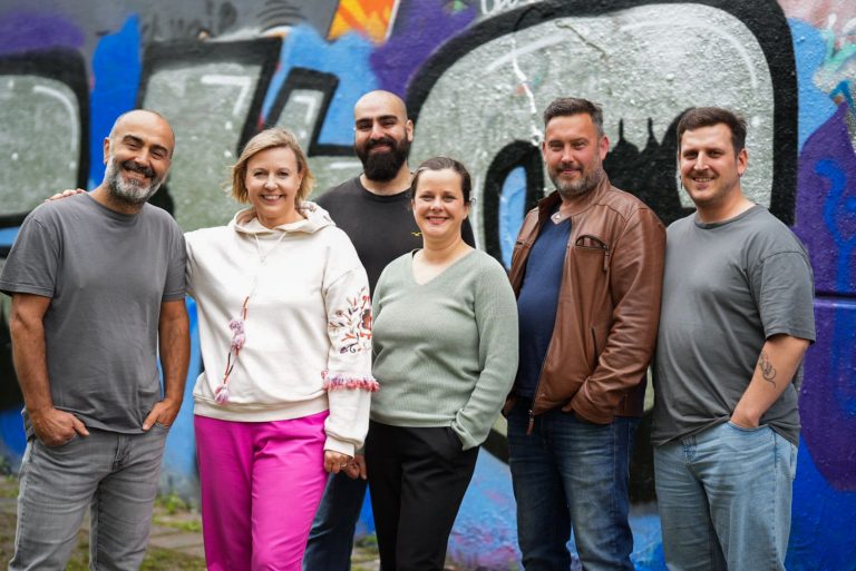 Das Projektteam steht vor einer bunten Graffiti-Wand