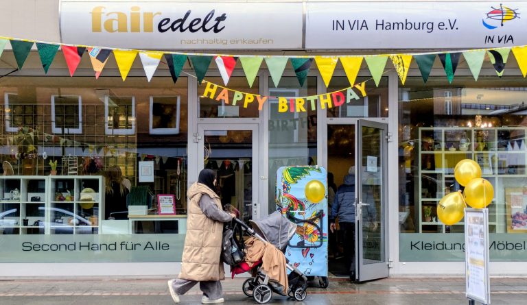 Eingang des Second-Hand Kaufhauses "fairedelt" festlich dekoriert mit Girlanden und Luftballons mit einer Kundin mit Kinderwagen