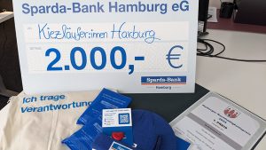 Spendenscheck über 2.000 Euro der Sparda-Bank Hamburg für die Kiezläufer:innen Harburg beim Nachhaltigkeitspreis, mit begleitenden Aktionsmaterialien