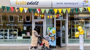 Eingang des Second-Hand-Ladens fairedelt in Hamburg mit Dekoration Happy Birthday und Besucherin mit Kinderwagen